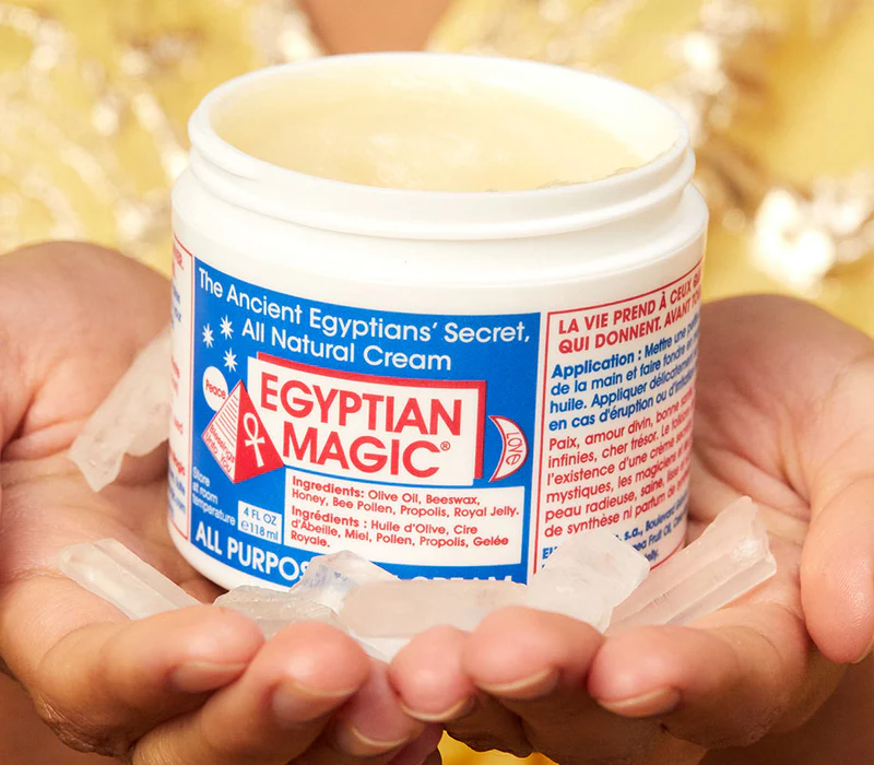 Egyptian Magic skin cream picture with open cap and hands holding the jar